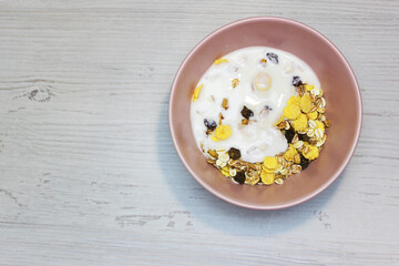 muesli with on a pink plate, top view. Muesli with fresh milk, yogurt or kefir. Muesli is made from oatmeal, a mixture of multi-grain flakes with dried fruits, nuts and sunflower seeds. on a white