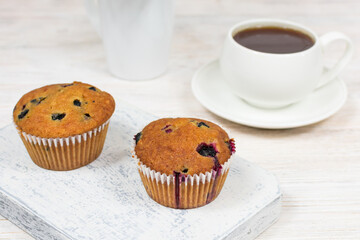 Delicious muffins with black currants close-up on a white wooden board on the background of a cup.