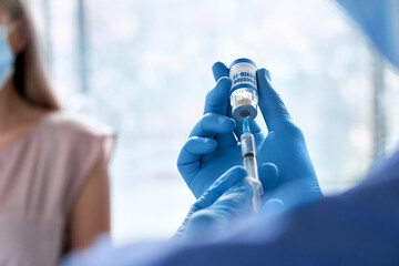 Male doctor wearing gloves holding syringe taking coronavirus vaccine dose from vail preparing for covid 19 vaccination for patient. Flu influenza vaccine clinical corona virus treatment close up view
