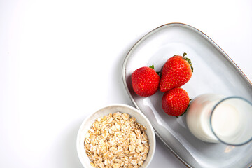 gray beautiful tray with strawberries and a glass of milk and a white bowl with oatmeal on a white table. Shooting from top to bottom. Flat composition. Horizontal photo with free space for text