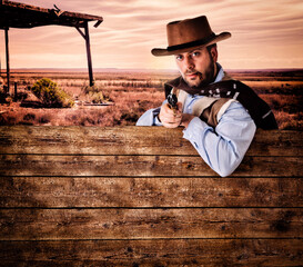 Gunman in the old wild west leaning on an empty wooden plank. - obrazy, fototapety, plakaty