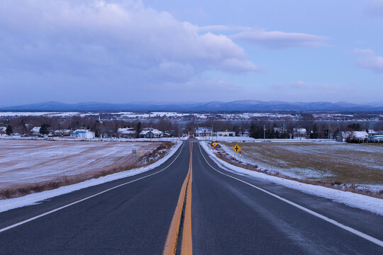 
Winter rural landscape with high angle view of route 281 running towards the St. Lawrence River coast seen during a blue hour morning, Saint-Michel-de-Bellechasse, Quebec, Canada