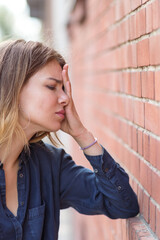 sad looking woman holds her head against a brick wall. Selective focus.