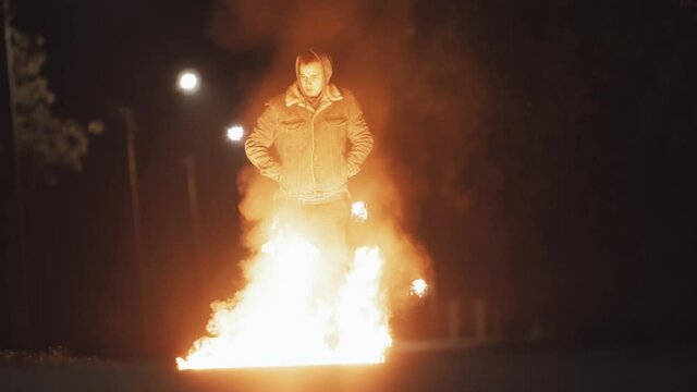 Pretty man in denim jacket uses matches to burn a gas puddle on asphalt. it causes a big fireball.