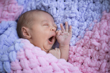 Newborn baby yawns and lies on a pink blanket