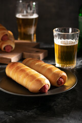 Sausages in the dough on a gray plate and two glasses of beer