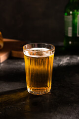 A glass of light beer with foam on a black table