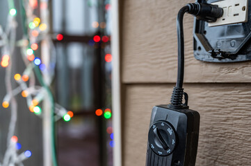Outdoor timer and GCFI outlet with cover. Blurred christmas lights in background.