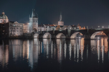 Fototapeta na wymiar illuminated Charles Bridge from 14 centuries and light from street lighting and stone sculptures on the bridge and light reflections on the surface of the Vltava river at night in Prague