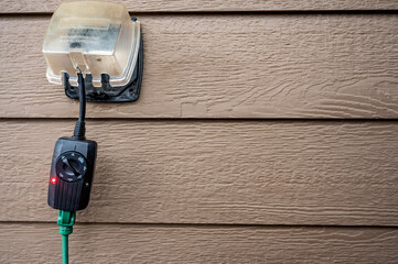 Outdoor timer and GCFI outlet with cover.  Brown siding on residential building