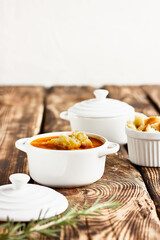 Vegetarian spicy autumn pumpkin cream soup served in white cocotte with croutons and pumpkin seeds on wooden table. Seasonal autumn vegetarian food.