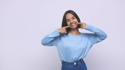 Young mixed race woman smiles, pointing fingers at mouth