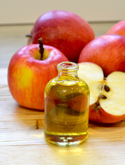 Apple cider vinegar in glass bottle and fresh apples on wooden background