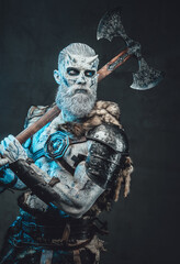 Shirtless eternal king of the dead with horns and blue eyes and two handed axe on his shoulder in dark background.