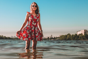 young brunette girl in a red dress kneeling in the water in the river