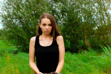 Naklejka na ściany i meble sad brunette girl in a black T-shirt stands in the field and looks from under his forehead