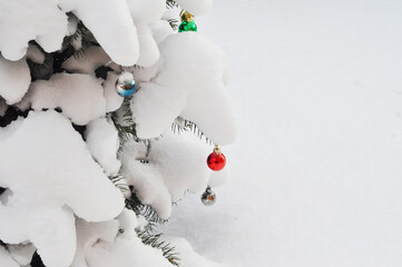 A close-up of a Christmas tree outdoors with branches heavily covered with snow and decorated with...