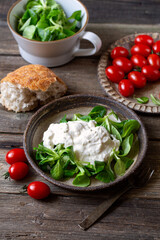 Stracciatella cheese  with salad corn and cherry tomatoes on handmade plate, wooden table.