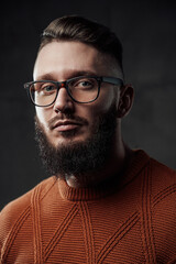 Obraz premium Bearded manly hipster with stylish hairstyle and beard posing in dark background weared with glasses.