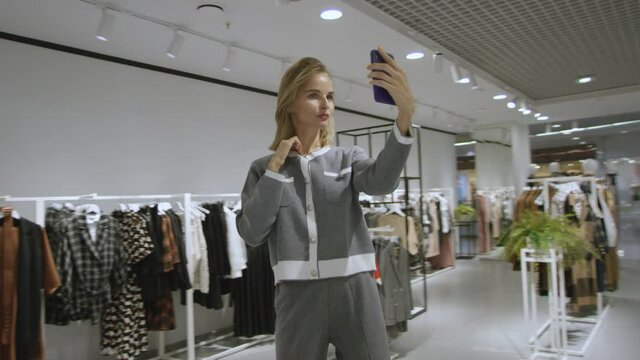Young happy beautiful woman is taking a photo of herself dressed in grey suit at clothing store, tracking shot, 360 degree
