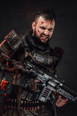 Fototapeta na wymiar Apocalyptic serious soldier dressed in dirty dark armour poses in dark background with angry face holding shotgun.