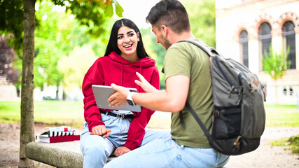 Two students studying together with a digital tablet sitting on a bench outdoor