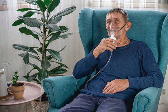 elderly senior sits in a armchair with an oxygen mask in quarantine at home