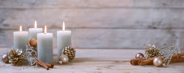 Four burning candles and Christmas decoration like cones, cinnamon and baubles against a rustic wooden background in pastel colores, copy space, panoramic format