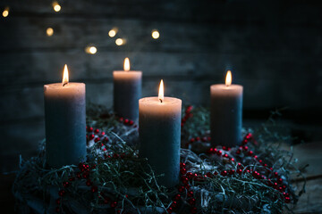 Four burning candles on an advent wreath with red Christmas decoration, tradition to bring light in...