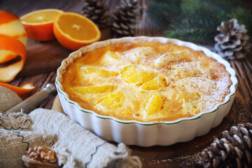 New Year dessert. Orange clafoutis with praline, powdered sugar dressing, spruce branch and pine cones decoration