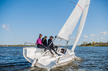 A beautiful white racing single-masted yacht is sailing against a beautiful river landscape with a...