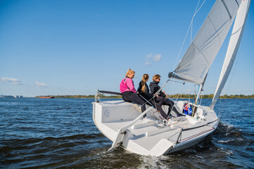Fototapeta premium A mixed crew of a sports yacht participates in sailing competitions on the river. One man and two girls