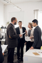 The Director of the company in a jacket gives instructions and tasks to young colleagues in the office of a trading company