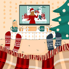 Couple, friends or family are watching Christmas and New Year movies on the bed in knitted socks, under plaid. Room is decorated in green, peach, white colours. Christmas tree in near the TV table