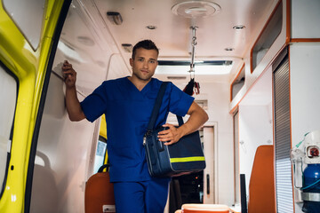 Paramedic in a blue uniform getting out of an ambulance car with a medical bag. © Anna Kosolapova