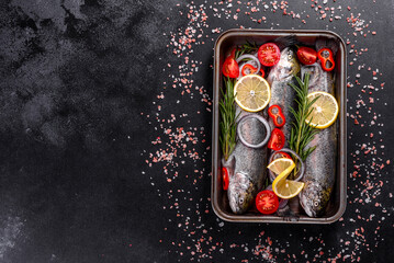 Raw trout lie on a black stone chopping board on a dark concrete table