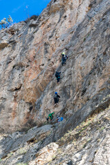 Several people climbing a rocky wall with metal staples embedded in the stone, also called Via...