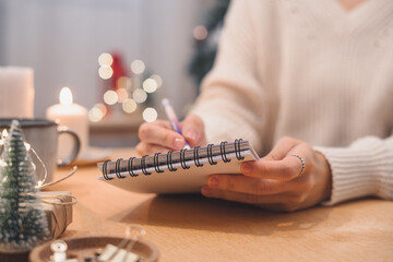 Goals plans make to do and wish list for new year christmas concept writing in notebook. Woman hand holding pen on notepad at home on winter holidays xmas. - obrazy, fototapety, plakaty