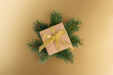 Gift box with ribbon and spruce branches on a golden background.