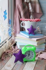 Clock, Christmas decorations, a cup of coffee with meringues, a stack of books, illumination on a wooden windowsill, a concept of home comfort
