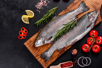 Raw trout lie on a black stone chopping board on a dark concrete table