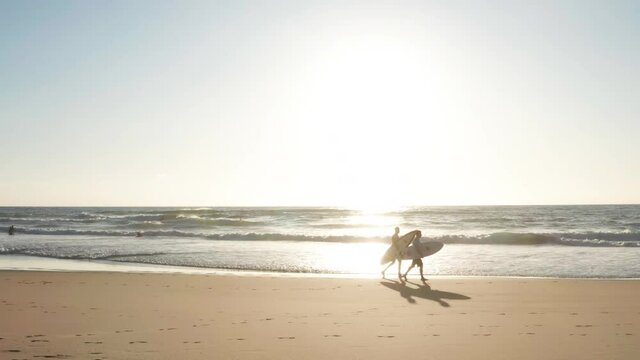 Surfers in backlighting at the ocean leaving the beach, view of people silhouette at the beach near Hossegor in France during a sunset