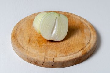 The onion is cut in half on a brown wooden board. The cutting board is on a white table.