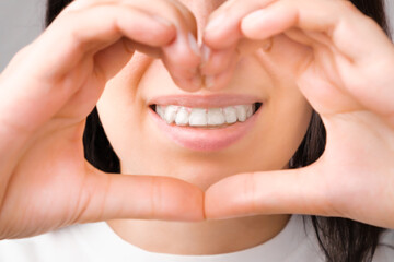 Happy woman with a perfect smile in transparent aligners on her teeth shows Heart with hands....