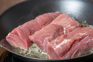 Three cleaned raw pieces of pork tenderloin are roasted in a pan.