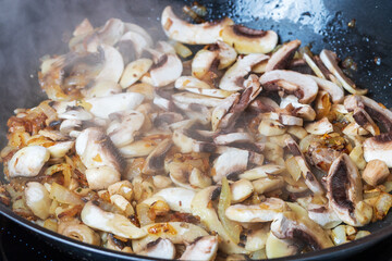 Sliced champignon mushroom is sautéed on onion in a pan.