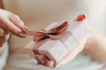 Obraz na płótnie Canvas Close-up of female hands holding a small gift wrapped with a satin ribbon