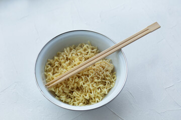 Instant noodles in a bowl with wooden chopsticks on a white textured background.