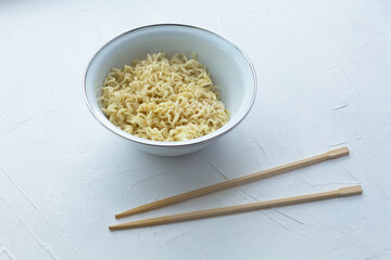 Instant noodles in a bowl with wooden chopsticks on a white textured background.