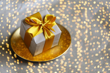 Gift box wrapped by kraft paper with yellow satin ribbon on gold handmade plate on bright shining background. Universal Christmas design